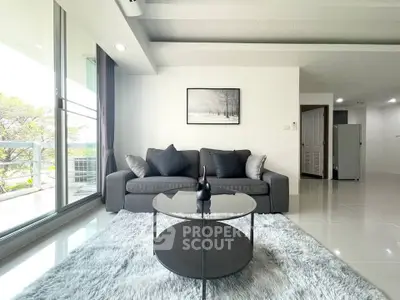 Modern living room with sleek gray sofa, glass coffee table, and large windows overlooking balcony.