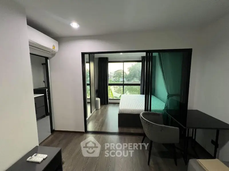 Modern studio apartment with bedroom and workspace, featuring large windows and sleek design.