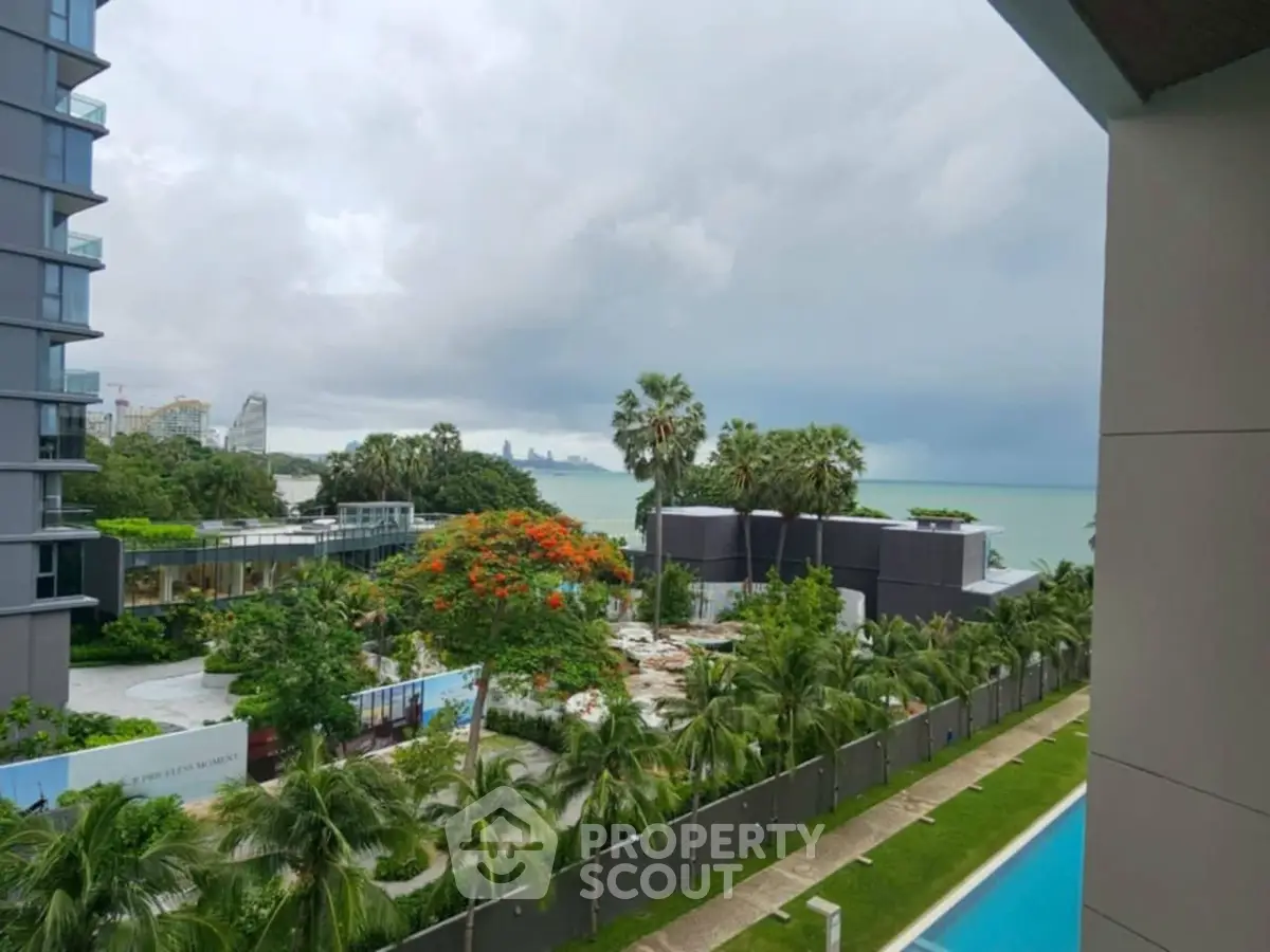 Stunning coastal view from modern apartment with lush greenery and poolside amenities.