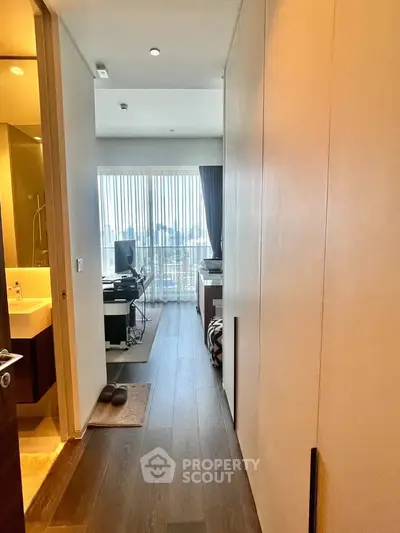 Modern apartment hallway leading to a bright bedroom with city view, featuring sleek wooden flooring and elegant decor.