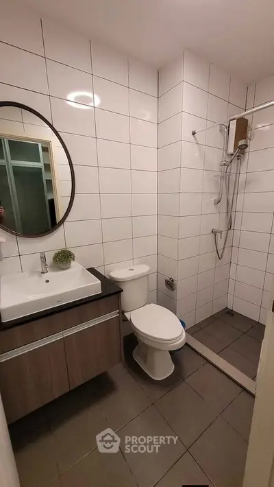 Modern bathroom with sleek design, featuring a round mirror, white tiles, and a glass shower enclosure.