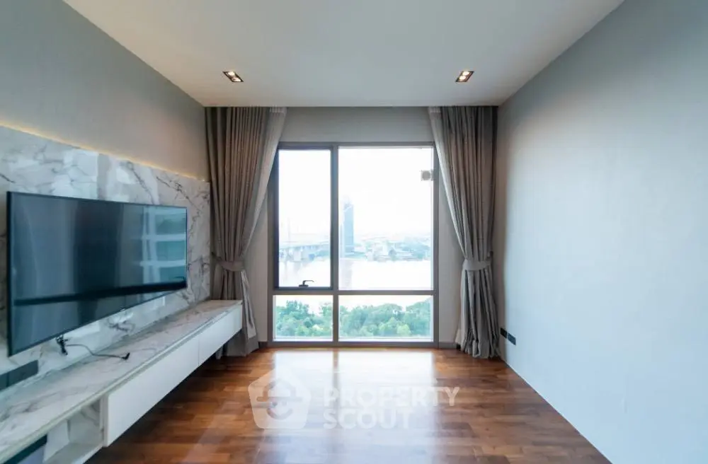Spacious living room with large window offering stunning city view, featuring modern TV setup and elegant curtains.