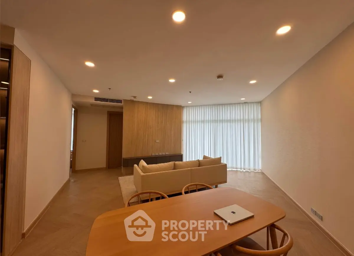 Spacious modern living room with elegant wooden dining table and cozy sofa, ideal for relaxation.