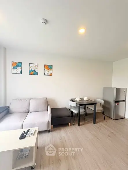 Modern living room with cozy sofa, dining table, and sleek fridge in open layout apartment.