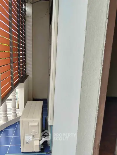 Compact balcony with air conditioning unit and wooden slat privacy screen.
