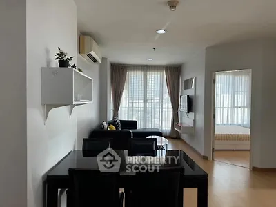 Modern open-plan living room with dining area and bedroom view, featuring sleek furniture and natural light.