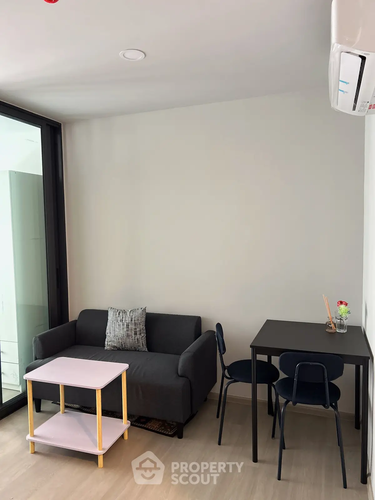 Modern living room with compact sofa, sleek table, and air conditioning in a cozy apartment setting.