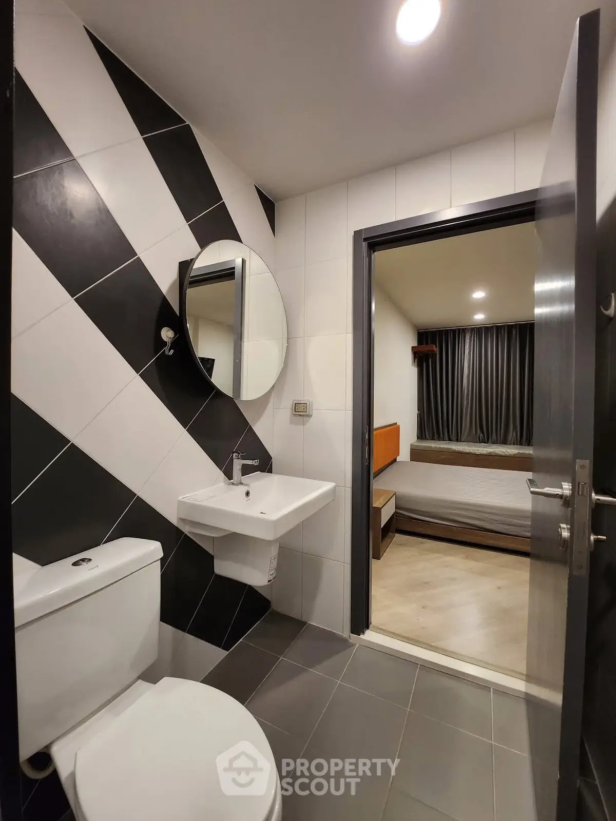Modern bathroom with stylish black and white tiles, featuring a sleek sink and toilet, leading to a cozy bedroom.