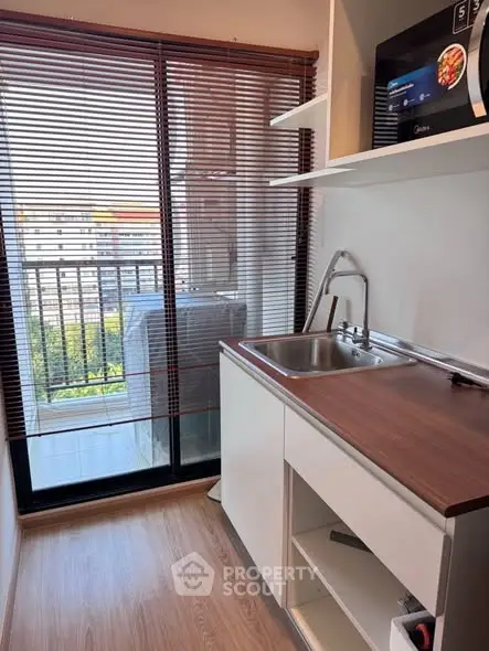 Compact kitchen with balcony view and modern appliances in urban apartment.