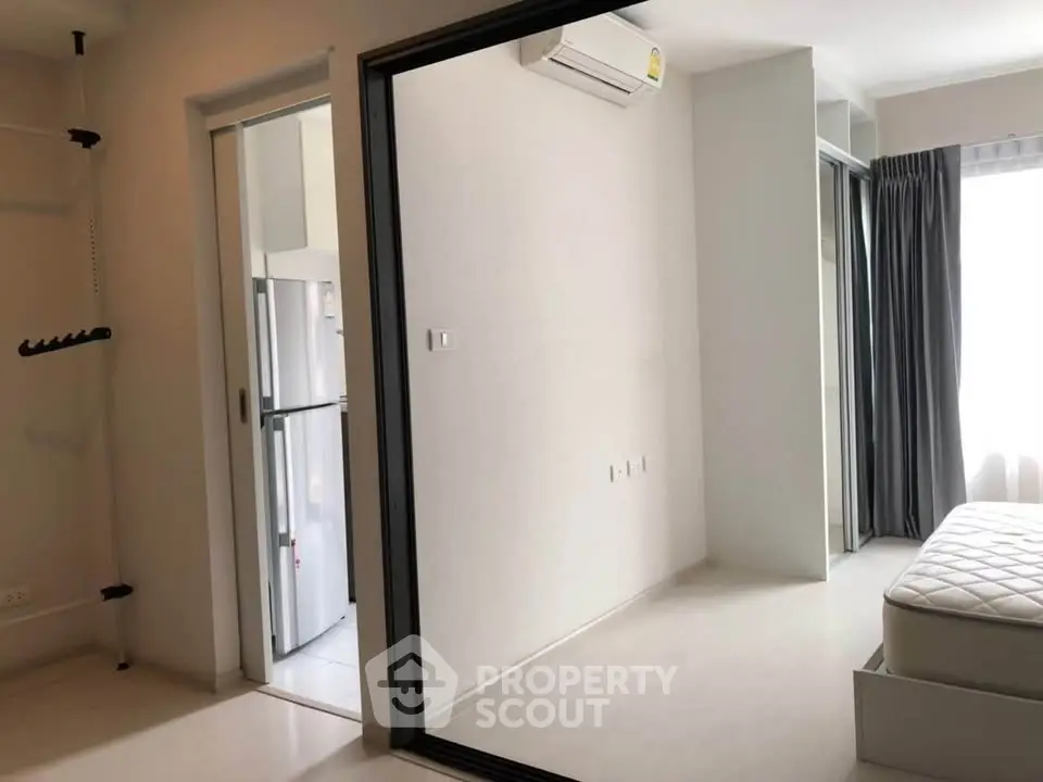 Modern minimalist bedroom with sliding glass door and air conditioning, adjacent to a sleek kitchen area.