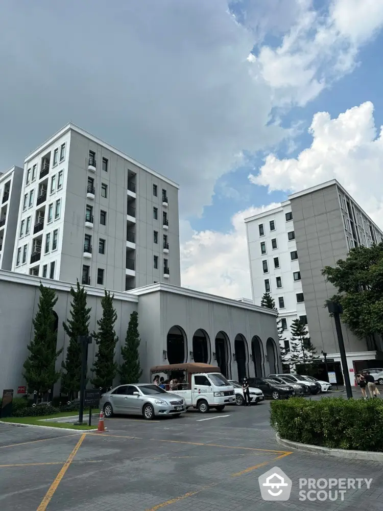 Modern residential building with parking and lush greenery under a blue sky.