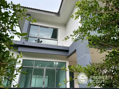 Modern two-story house with large windows and lush greenery