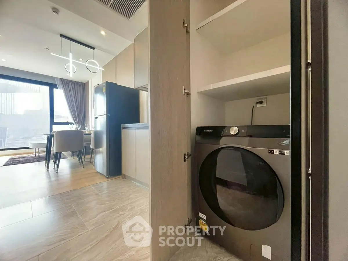 Modern apartment with sleek kitchen and built-in laundry area, featuring contemporary lighting and large windows.