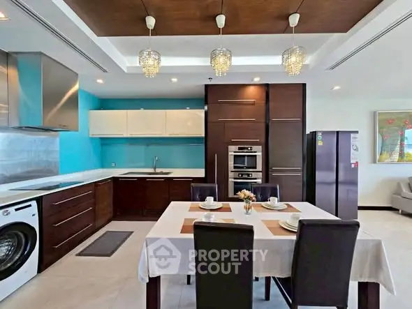 Modern kitchen with dining area, featuring sleek cabinetry, washing machine, and elegant lighting.
