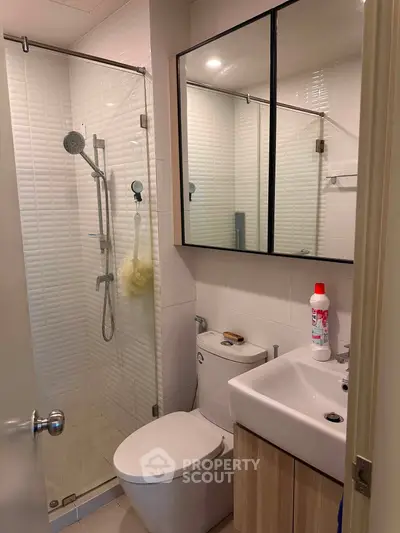 Modern bathroom with glass shower, sleek vanity, and mirrored cabinet in a contemporary apartment.
