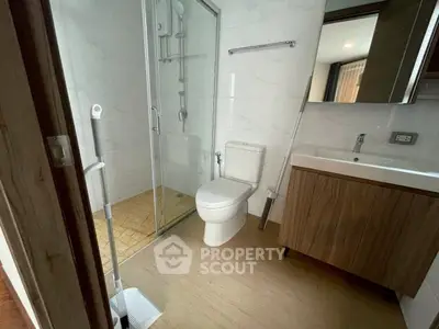 Modern bathroom with glass shower and wooden vanity in sleek apartment.