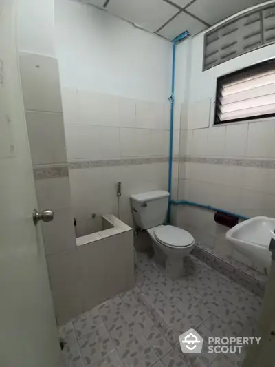 Functional bathroom with white tiling, toilet, bidet, and small window for natural light, ideal for a practical home renovation.