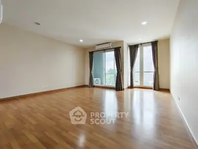 Spacious empty living room with wooden flooring and large windows.