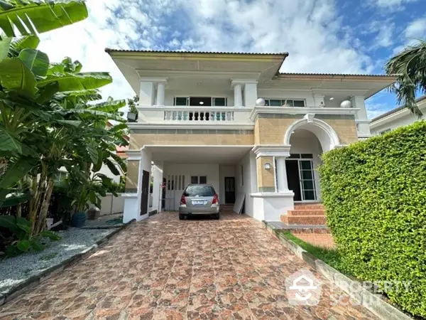 Elegant two-story residence with a spacious driveway and lush greenery, featuring a grand entrance and a serene balcony, nestled in a tranquil neighborhood.