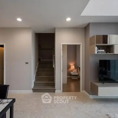 Modern living room with staircase and stylish decor, featuring a wall-mounted TV and elegant lighting.