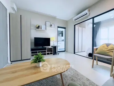 Modern living room with sleek furniture and open layout, featuring a cozy bedroom view through sliding glass doors.