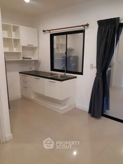 Modern kitchen with sleek white cabinets and black countertop in a cozy apartment.
