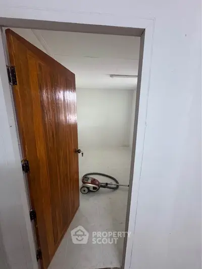 Spacious room with wooden door and vacuum cleaner, ideal for versatile use.