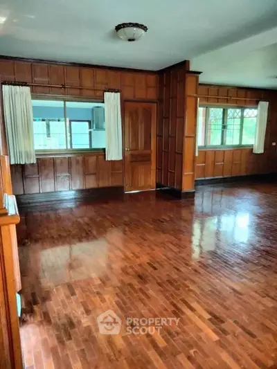 Spacious living room with polished wooden floors and large windows in a classic home.