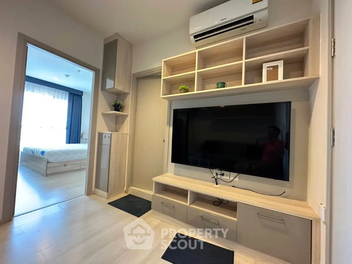 Modern living room with built-in TV unit and air conditioning, leading to a cozy bedroom.