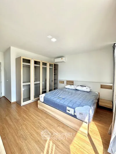 Spacious bedroom with modern wooden flooring and ample natural light, featuring a large bed and built-in wardrobe.