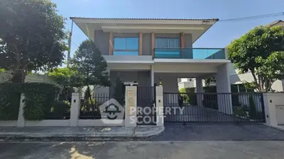Modern two-story house with large balcony and gated entrance in lush neighborhood