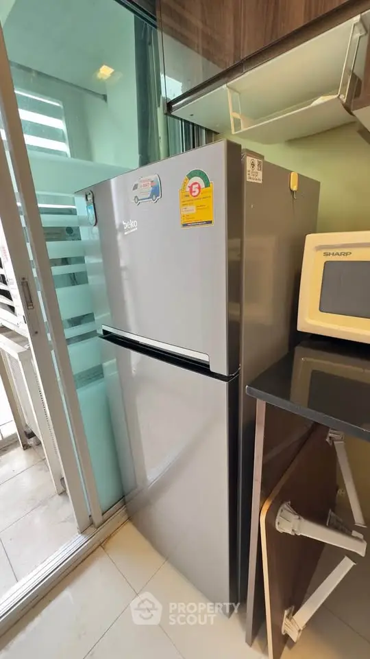 Modern kitchen with stainless steel fridge and microwave, sleek cabinetry, and balcony access.