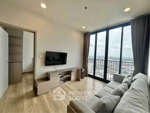 Modern living room with large windows and city view, featuring a cozy sofa and wall-mounted TV.