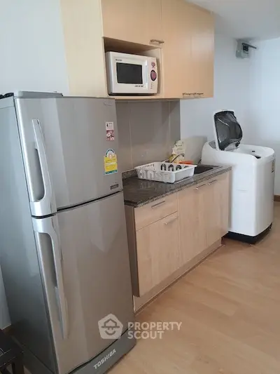 Modern kitchen with stainless steel fridge, microwave, and washing machine in compact layout.