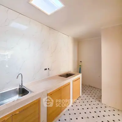 Modern kitchen with marble backsplash and skylight, featuring wooden cabinets and tiled flooring.