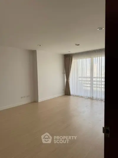 Spacious empty room with large window and wooden flooring, ideal for customization.