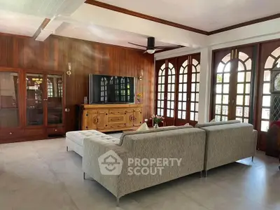 Spacious living room with modern sofa and large TV, featuring elegant wooden accents and natural light.