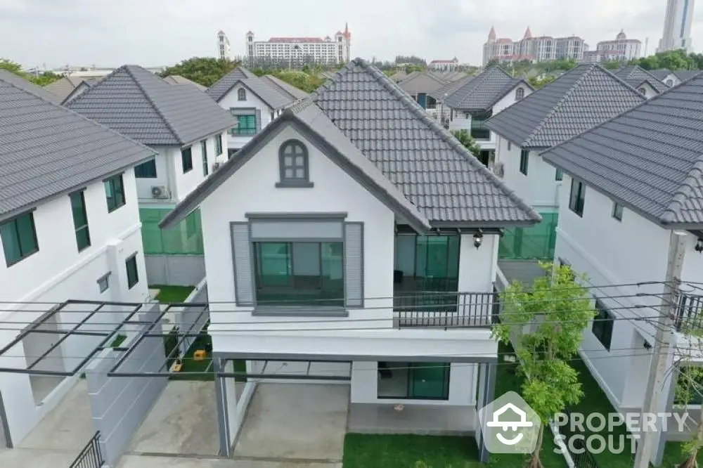 Elegant two-story house with a gray gable roof and a charming balcony, nestled in a peaceful suburban neighborhood with lush greenery.