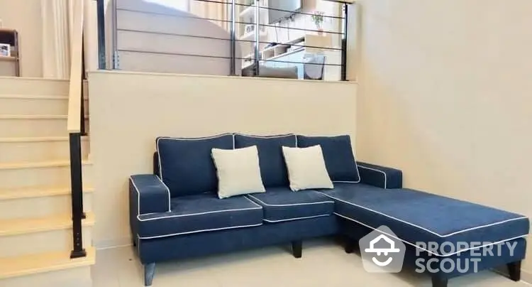 Elegant living space featuring a plush blue sectional sofa with chic accent pillows, adjacent to a modern staircase with sleek metal railings.