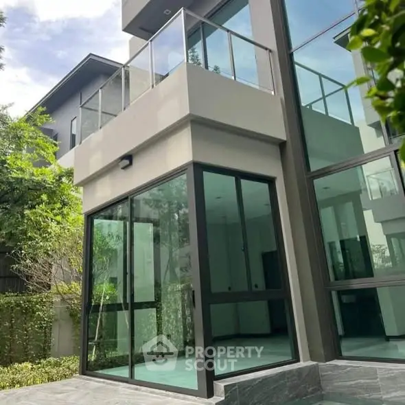 Modern glass facade of luxury home with spacious balcony and lush greenery.