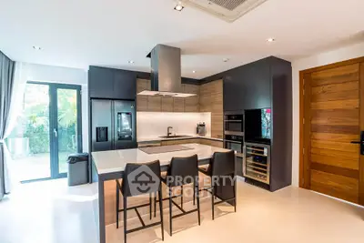 Modern kitchen with sleek black cabinets, island seating, and stainless steel appliances in a bright open layout.