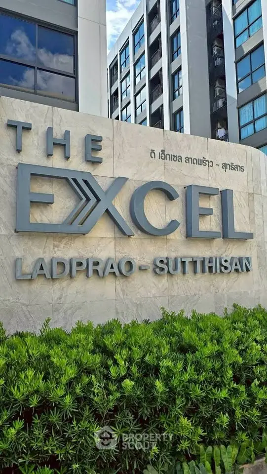 Modern apartment building exterior with lush greenery and prominent signage.