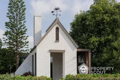 Charming white brick house with unique roof design and lush greenery