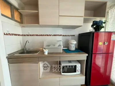 Modern kitchen with red fridge, microwave, and sleek cabinetry in a compact layout.