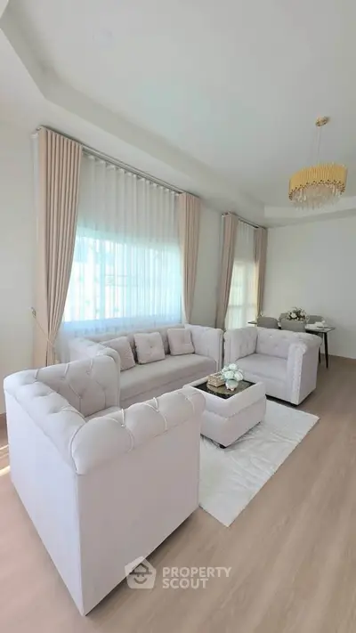 Elegant living room with plush white sofas, chic chandelier, and soft natural light for a luxurious ambiance.