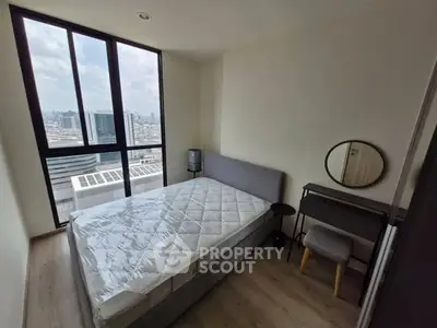 Modern bedroom with large windows offering city views, featuring a stylish bed and compact workspace.