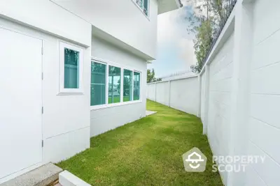 Modern white exterior with lush green lawn and privacy wall