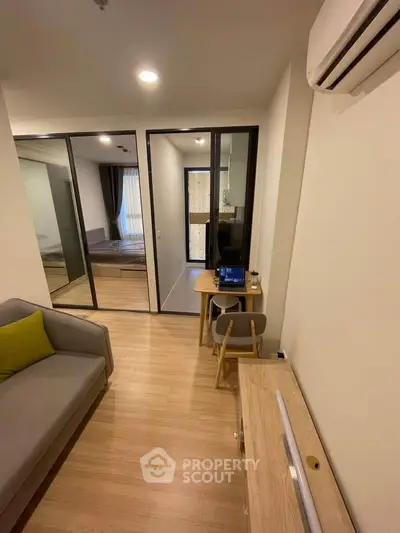 Modern apartment interior with cozy living room and bedroom view, featuring sleek furniture and wooden flooring.