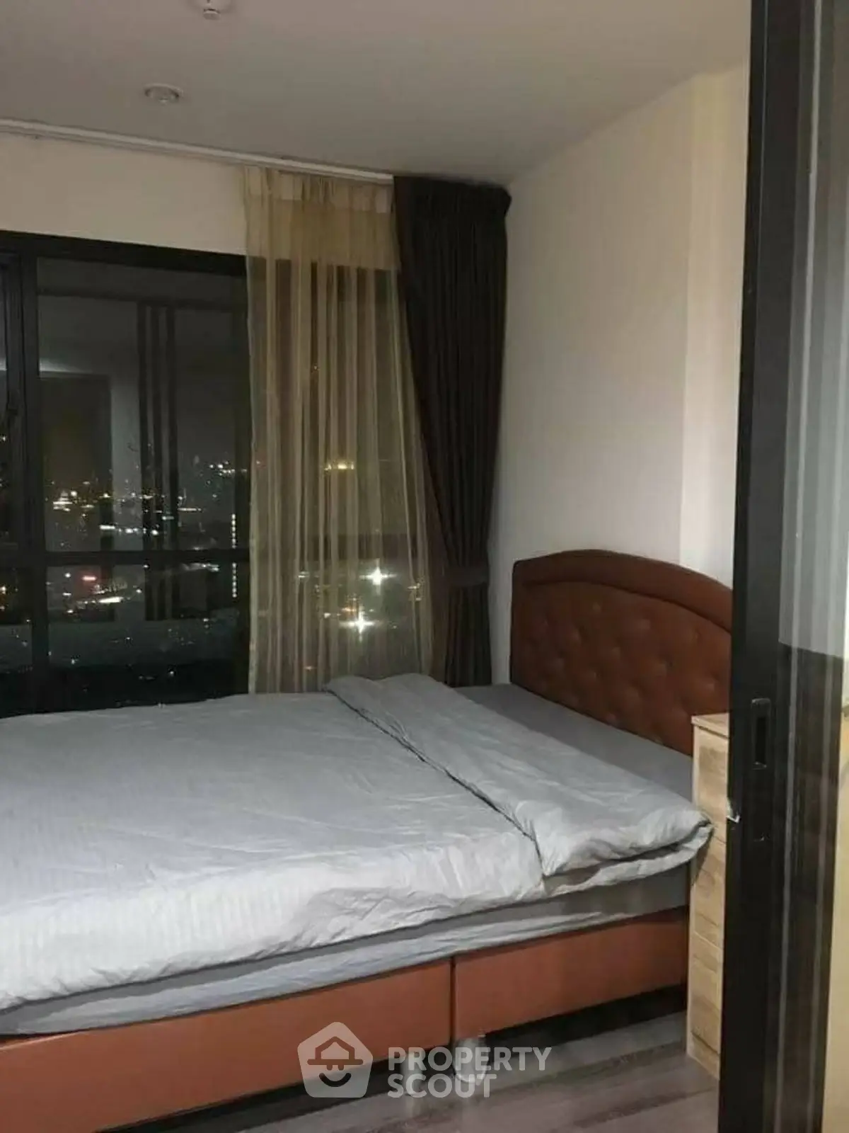 Cozy bedroom with city view, featuring a comfortable bed and elegant curtains.