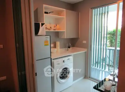 Modern kitchen with washing machine and fridge, featuring sleek cabinetry and sliding glass door to balcony.